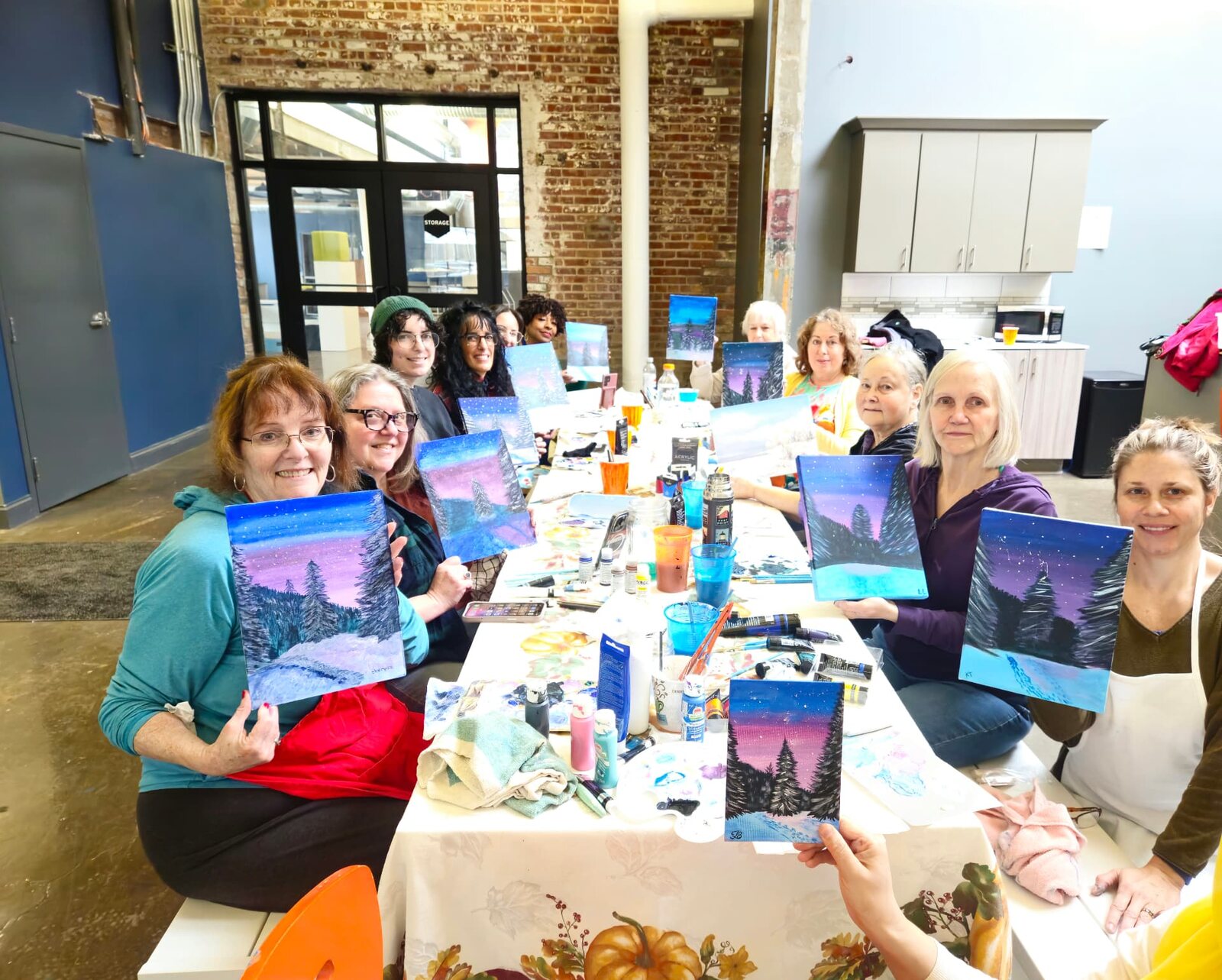 Adult art students smiling together and showing the winter paintings they completed in class