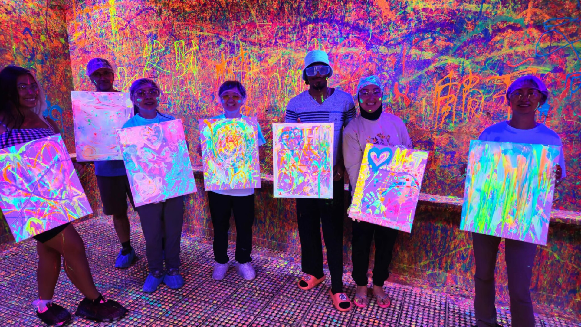 A group of adult students holding their colourful paintings in a neon art class